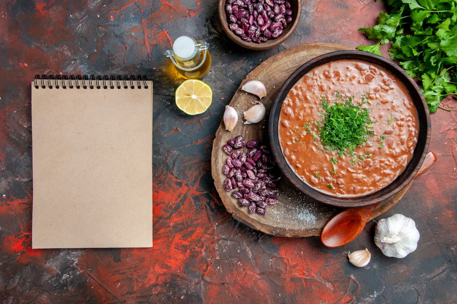 Rustic Purple Black Bean Soup Recipe garnished with fresh herbs, surrounded by raw beans, garlic, lemon, and olive oil on a textured background, perfect for your culinary inspiration.