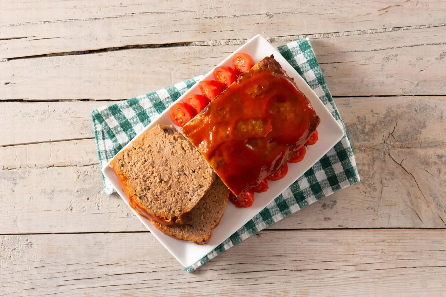 Delicious meatloaf recipe Lipton onion soup mix, topped with a tangy glaze and served with fresh cherry tomatoes on a rustic wooden table.