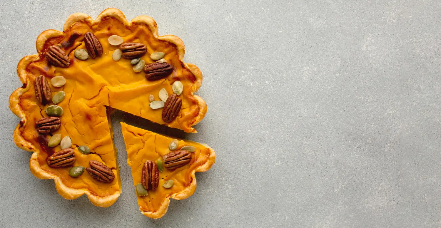 Golden Two-Crust Sweet Potato Pie topped with pecans and pumpkin seeds, with a slice removed, showcasing its creamy texture.