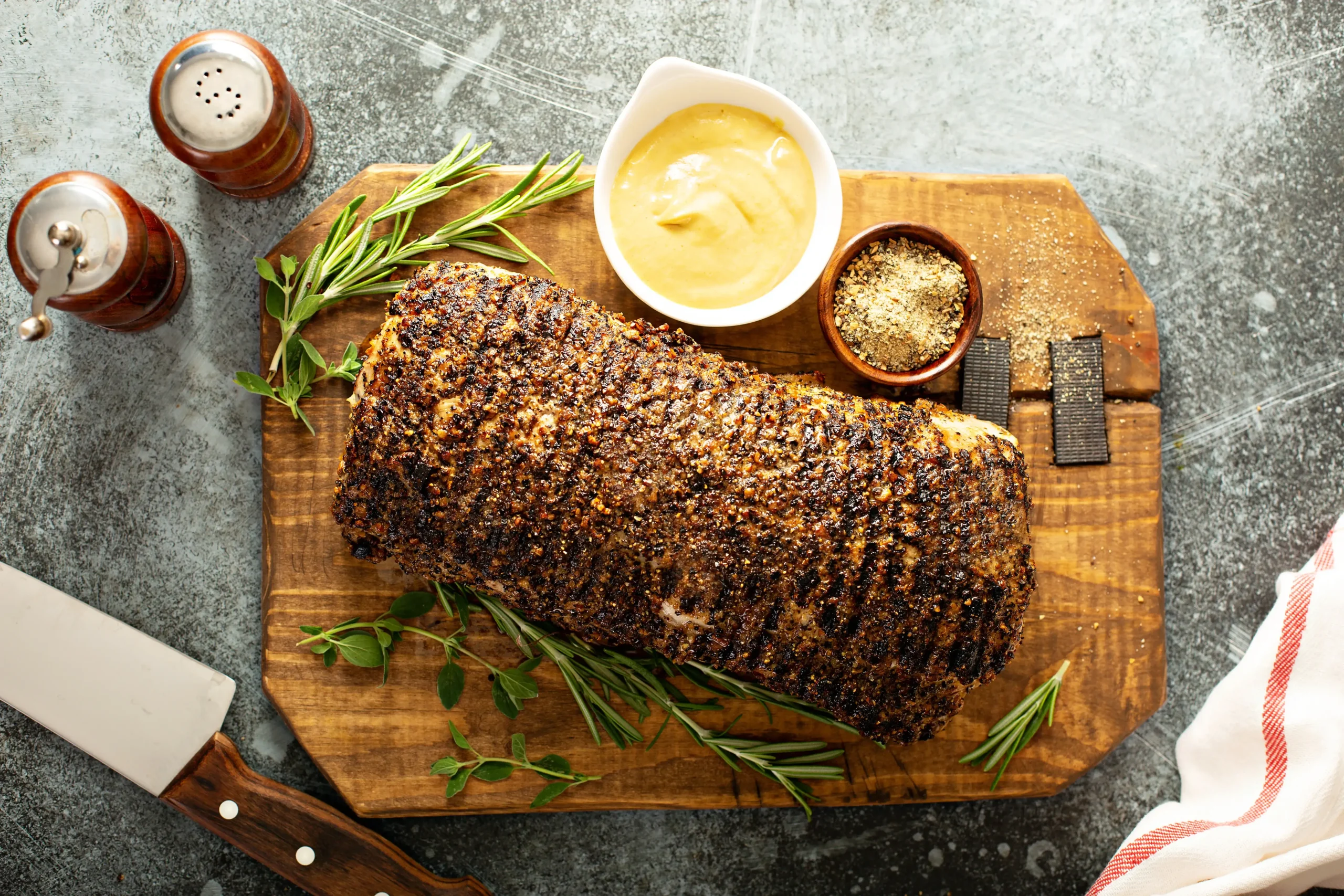 Prime Rib roast seasoned with a flavorful crust, served on a wooden cutting board with fresh herbs, mustard, and spices, perfect for elevating any meal.